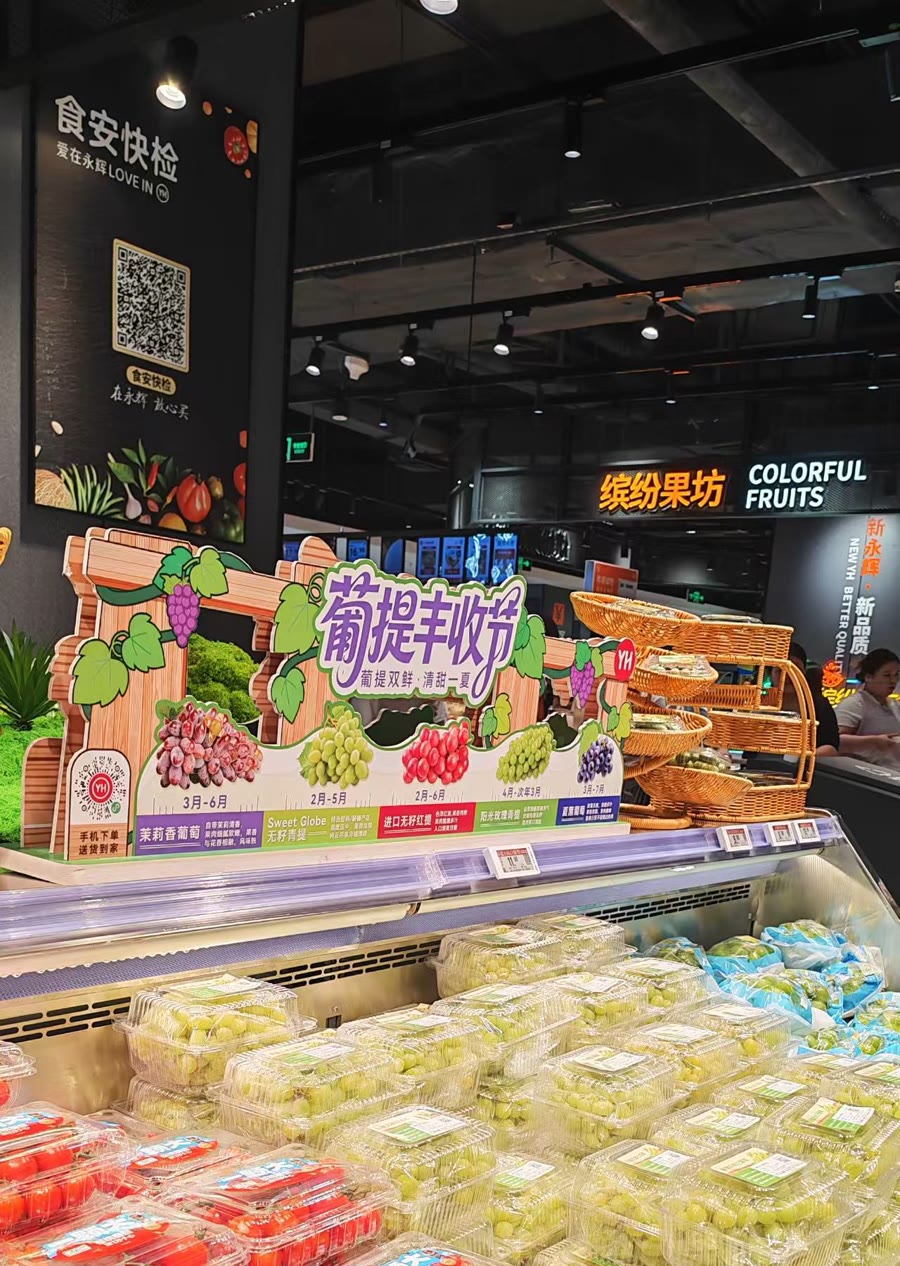 超市水果区：食安快检立牌与葡提丰收节档期牌，下方是满陈列的预包装葡萄
